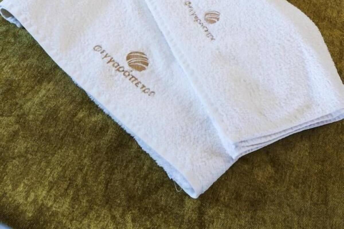 Un lit bien fait, avec du linge de lit blanc et des oreillers, une serviette verte ornée d’un logo, et un mur blanc en arrière-plan.