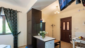 A compact kitchen with a refrigerator, a dining table with chairs, a small bench, and a TV mounted on the wall. - Fegaropetra studios (Igoumenitsa)