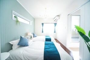 Two single beds with white bedding and blue accents, a chandelier, and a potted plant create a comfortable and airy space.