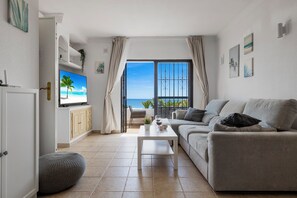 Relax in this stylish living room with a large flat-screen TV, comfortable sofa, and ocean views from the balcony.