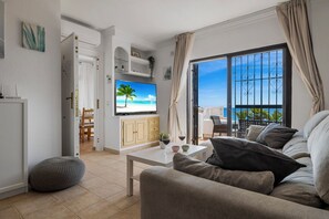 Relax in a spacious living room with a sofa, coffee table, and flat-screen TV, offering a view of the sea from the large window and balcony.