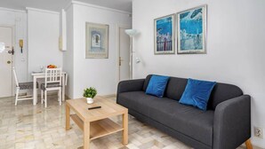 A living room with a grey sofa, a wooden coffee table, and a white dining table with chairs. There are two framed artworks on the wall and a floor lamp. - Relaxing Getaway by Costarentals - Ref 169 (Fuengirola)