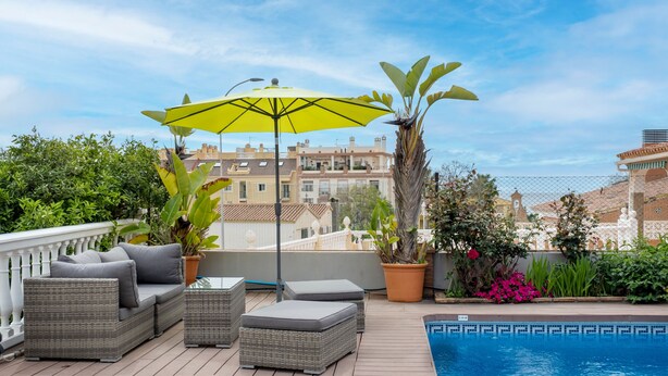 Una terraza en la azotea con mobiliario de mimbre, una piscina y plantas en macetas.