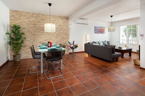 A dining area with a brick wall, a table with chairs, a sofa, and a window with a view.