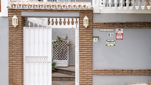 Una entrada protegida con un portón blanco, un muro de ladrillo y un piso de baldosas.