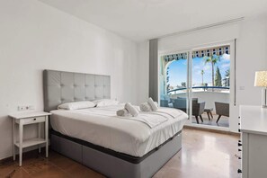 Habitación de hotel moderna con una cama grande, una mesita de noche pequeña y vistas al área exterior a través de un ventanal corredero.