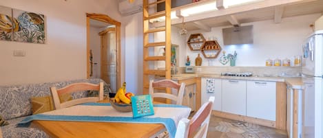 Una cocina acogedora con armarios de madera, una mesa de comedor con sillas y una escalera que lleva a una zona superior.
