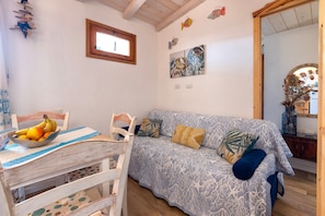A room with a wooden ceiling, a dining table with a bowl of fruit, a patterned sofa, and a wall with artwork.