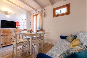 A living room with a TV, wooden dining table, chairs, and a sofa with patterned cushions.
