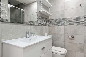 Une salle de bain moderne avec un grand miroir, un lavabo blanc et des toilettes.