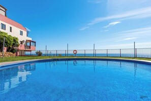 Une piscine avec vue sur la mer, un panneau indiquant qu’il est interdit de plonger, et un bâtiment avec un toit rouge.