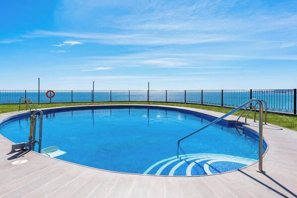 Une piscine offrant une vue dégagée sur l’océan, entourée d’une clôture et dotée d’une terrasse carrelée.