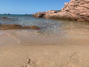 A beach with clear water, rocky formations, and a sandy shore.