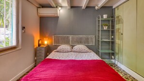 A bedroom with a bed, bedside table, lamp, and a window with blinds. - Oasis Centre Charme House with Shared Pool, Wi-Fi, and Air Conditioning (Montpellier)