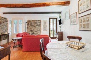 Une pièce avec un plafond en bois, des murs en pierre, un canapé rouge, un lit avec une tête de lit en bois et des tableaux encadrés accrochés au mur.