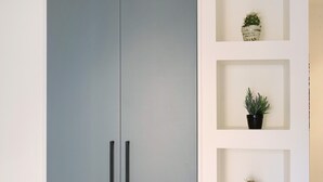 A modern interior with a grey cabinet, a white shelf with three potted plants, and a small decorative item. - ‘Victoria Family’ Apartment with Balcony, Wi-Fi & Air Conditioning (Diano Marina)