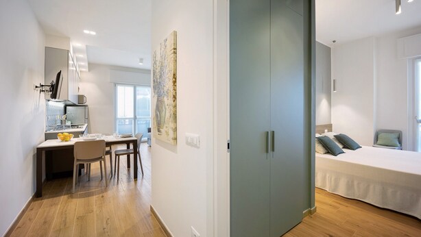 A modern hotel room with a bed, a desk with a chair, a dining table, and a large wardrobe. - ‘Victoria Family’ Apartment with Balcony, Wi-Fi & Air Conditioning (Diano Marina)