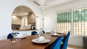 A dining area with a wooden table set for four, blue chairs, and a view of a stone wall through a window. - 'Villa In Los Flamencos' with Private Pool, Wi-Fi and Air Conditioning (Mijas Costa, Riviera del Sol)