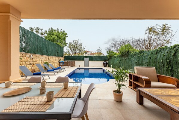 A pool area with lounge chairs, a dining table, and a sofa.