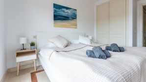 A neatly made bed with a white comforter, a bedside table with a lamp, a small plant, and a painting of a beach scene. - 'Villa In Los Flamencos' with Private Pool, Wi-Fi and Air Conditioning (Mijas Costa, Riviera del Sol)