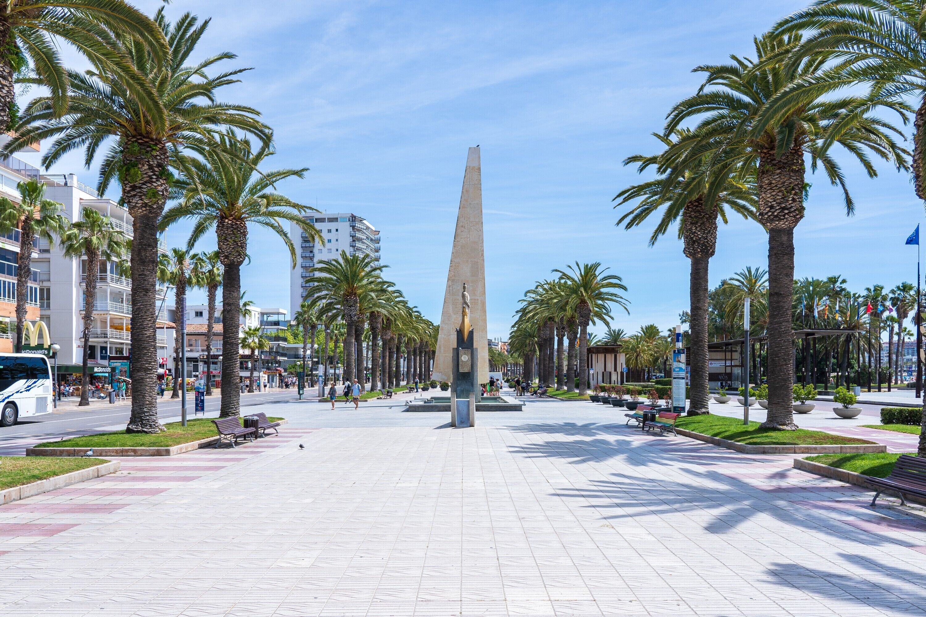 A public square with a tall obelisk, palm trees, benches, and a McDonald's restaurant.