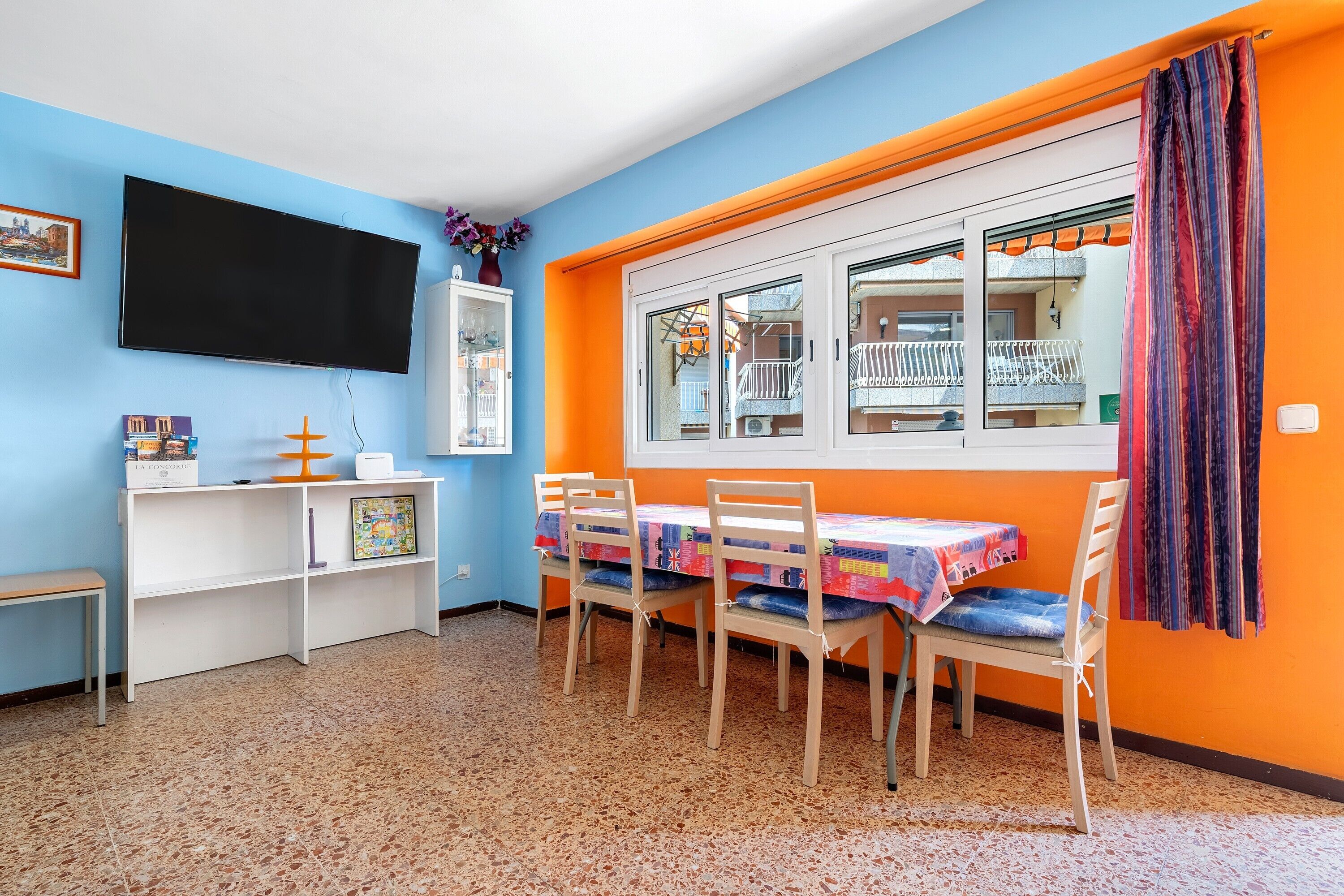 Una habitación con televisión, ventana con vistas, una mesa con sillas y una estantería.