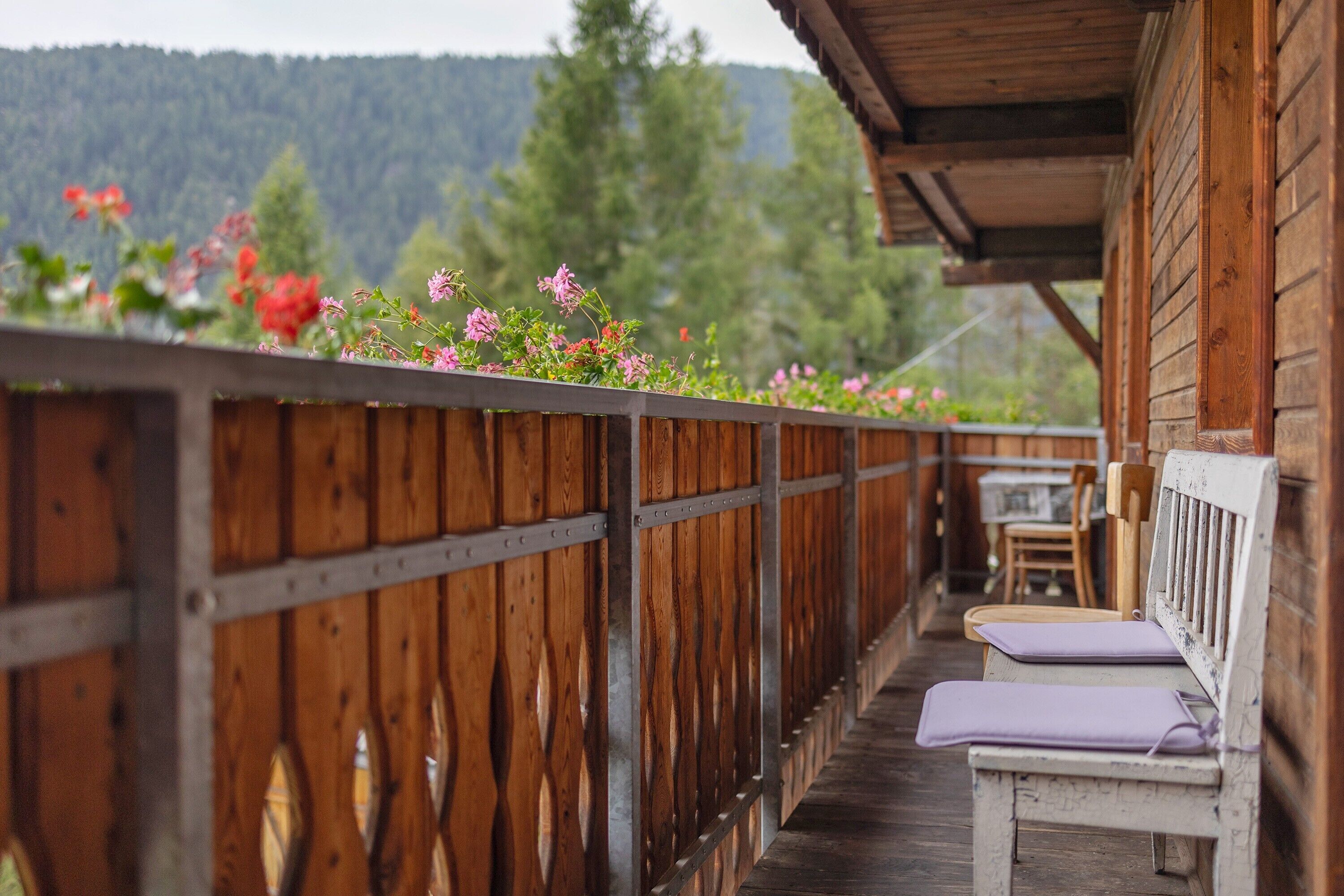 A wooden balcony with a bench and a table, surrounded by a wooden fence and flowers.