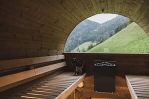 Un intérieur en bois avec un banc, une poubelle et une vue sur un paysage verdoyant, visible à travers une fenêtre semi-circulaire.