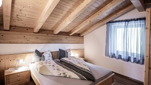 Une chambre avec un plafond en bois, un lit recouvert d’une couverture à rayures, une table de chevet avec une lampe et une fenêtre avec des rideaux.
