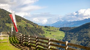 Une clôture en bois avec un drapeau, une vallée parsemée de maisons et des montagnes en arrière-plan.