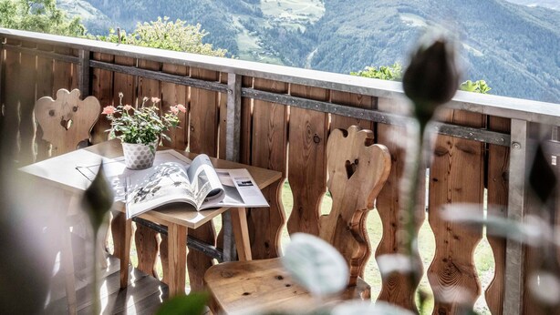 Une terrasse en bois avec une table, des chaises et un livre, offrant une vue sur un paysage montagneux.