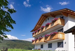 Ein mehrstöckiges Gebäude mit Holzbalkonen, die mit Blumen geschmückt sind, vor einer Bergkulisse.