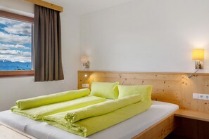 Ein Hotelzimmer mit einem hölzernen Kopfteil, einem Bett mit grünen Handtüchern, einem Fenster mit Vorhängen und einer Wandlampe.