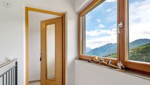 Een kamer met een houten deur, een raam met uitzicht op bergen en een klein plankje met beeldjes.