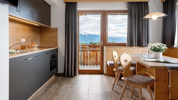 Een moderne keuken met een houten aanrechtblad, een inbouwoven en uitzicht op bergen door een glazen deur.