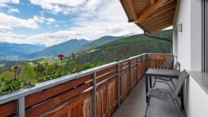 Een balkon met uitzicht op bergen, een tafel en stoelen.