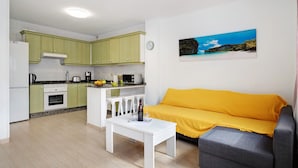 Un espacio habitable compacto con kitchenette, un sofá, una mesa de comedor y un cuadro en la pared.
