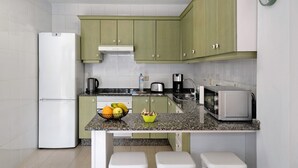 Cocina compacta con refrigerador, microondas, tostadora y un bol de fruta en la encimera.