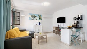 A modern living room with a sofa, a coffee table, a TV, and a kitchen area with a microwave and coffee maker.