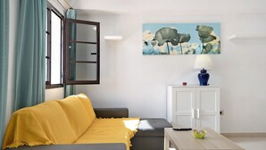 A living room with a sofa, a table, a cabinet, a painting, and a window with curtains.