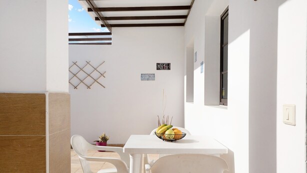 A small dining area with a white table and chairs, a fruit bowl, and a wall-mounted number plate.
