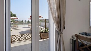 Un balcon donnant sur une piscine et des parasols, une chaise en bois, une table avec un ordinateur portable et une horloge au mur.