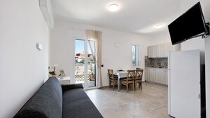 Un espace de vie compact comprenant un canapé, une table à manger avec des chaises, un coin cuisine et un téléviseur fixé au mur.