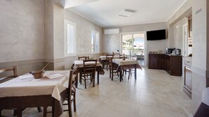 Un espace repas avec des tables et des chaises, un coin cuisine avec des placards et des appareils électroménagers, et un téléviseur fixé au mur.
