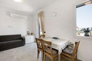 Una habitación con una mesa de comedor, sillas, un sofá, un armario pequeño, un reloj y una ventana con vistas.