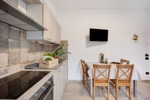 A modern kitchen with a built-in stove, wooden cabinets, a dining table with chairs, and a flat-screen TV mounted on the wall.
