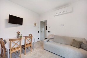 A living room with a flat-screen TV, a sofa, and a dining table with chairs.