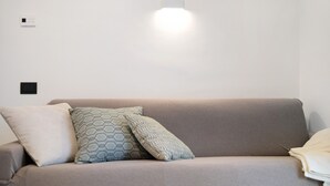 A neutral-toned sofa with patterned cushions, a wall-mounted light, and a power outlet. - Holiday Apartment "Antichi Ricordi - La Stalla" with Terrace, Shared Pool & Wi-Fi (Andora)