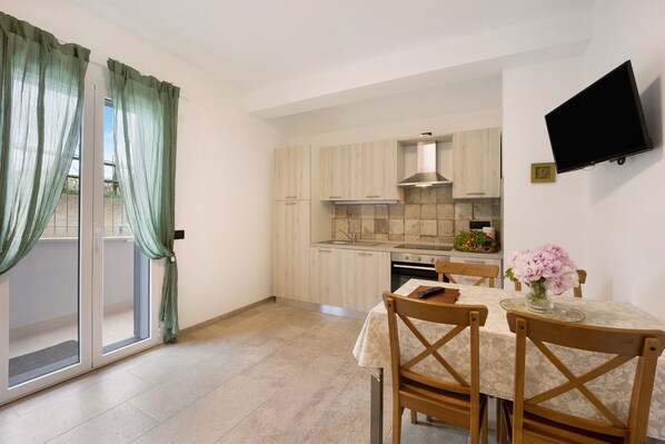 A modern kitchen with light wood cabinets, a stainless steel range hood, and a dining area with a table and chairs.