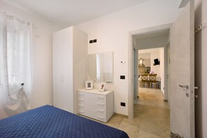A bedroom with a bed, dresser, mirror, and a view into the dining area.